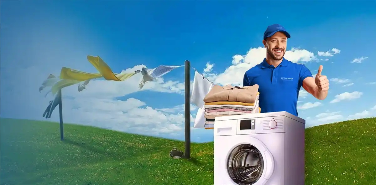 Smiling laundry professional showing thumbs up beside a washing machine with laundry baskets in an open blue-sky setting